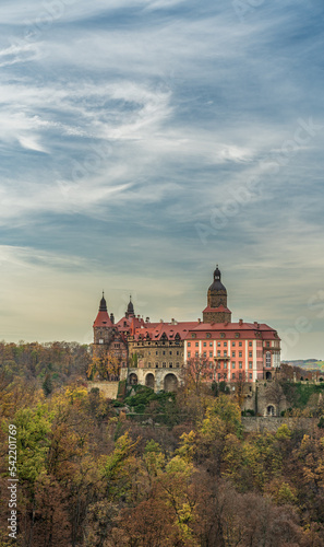 A photo of Książ Castle in Wałbrzych set against a beautiful autumn sky. The castle, with its impressive architecture, stands out against the picturesque background of the colorful fall foliage