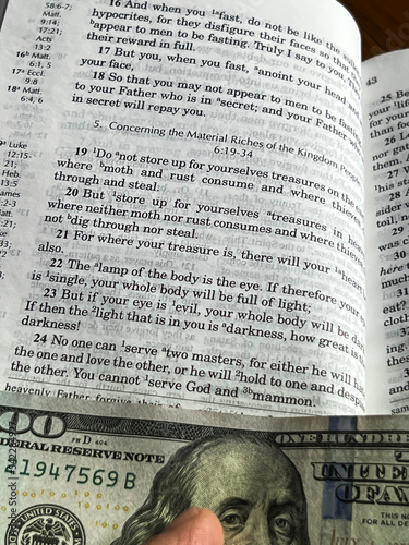 The Holy Bible in English with a tab from the $ 100 banknote showing a passage from the Gospel according to St. Matthew 6:24