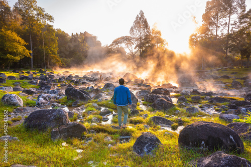 Male tourist standing and looking at Natural hot spring with steam, and rock in the morning at Chae Son National Park, Lampang, Thailand.