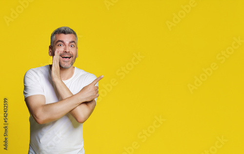 Handsome man pointing sideways making some secret talk with hands smiling looking at camera wearing casual isolated on yellow background. Happy freelancer man introduce mock up for business