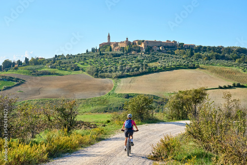 nice senior woman riding her electric mountain bike in the Ghianti area beow the skyline of the medieval city of Pienza , Tuscany , Italy