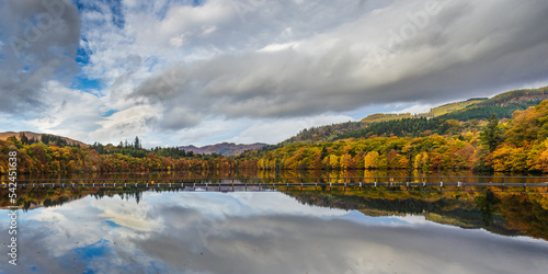 Peaceful water reflection of cloudy sky and autumn trees in Pitlochry