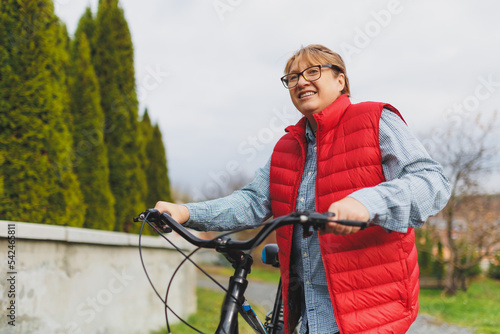Middle aged smiling mature woman holdingt a bike with her hands on the grass on a green field. Summer or Autumn Country Vacation and Adventure Concept