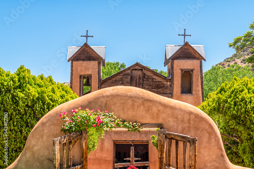 Famous historic adobe El Santuario de Chimayo sanctuary church in the United States with entrance gate closeup of flowers in summer