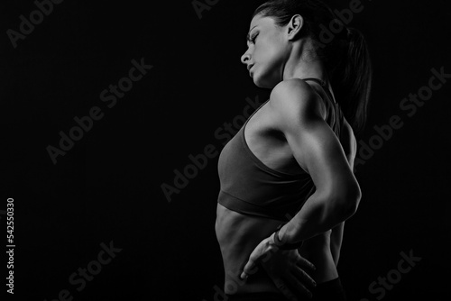 Sporty woman holding hands to relax the tension and pain in lower back and sacrum in sport top on empty copy space studio background. Back view. The concept of medicine.