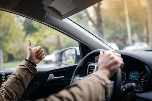 The driver behind the wheel of the car shows the gesture THUMB UP. Help and respect for safe transportation.