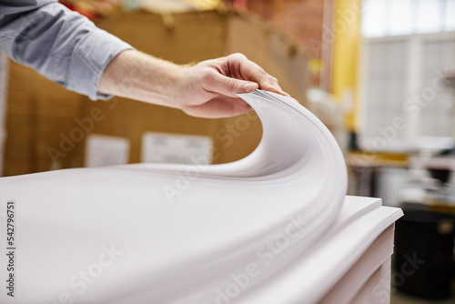 Close up of person checking quality of paper stack in printing shop, copy space