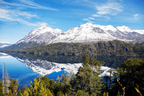 panorama of lago gutierrez with the mirrored lake on a sunny day, mountains with green forests. Snowy cathedral hill in the background