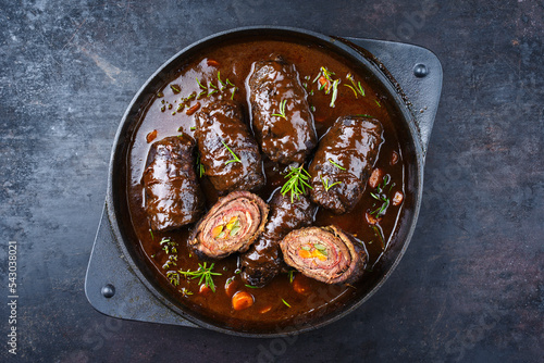 Traditional slow cooked German wagyu beef roulades with vegetable and bacon served in spicy gravy sauce as top view in a design pot with copy space
