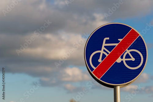 Znak drogowy : " koniec drogi dla rowerów " . Granatowy znak z przekreśloną ( białą) sylwetką roweru , na tle błękitnego nieba z białymi chmurkami . 