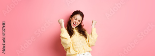 Girl screams with joy and fist pump, say yes, achieve goal or success, celebrating achievement, triumphing and winning, standing over pink background