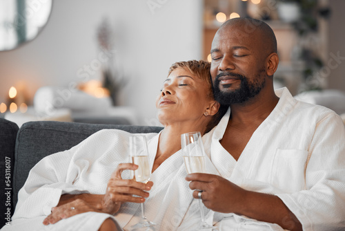 Mature couple, bonding and champagne on spa date, romantic retreat or resort holiday for marriage anniversary celebration. Black woman, man and alcohol glass on relax salon or hotel living room sofa