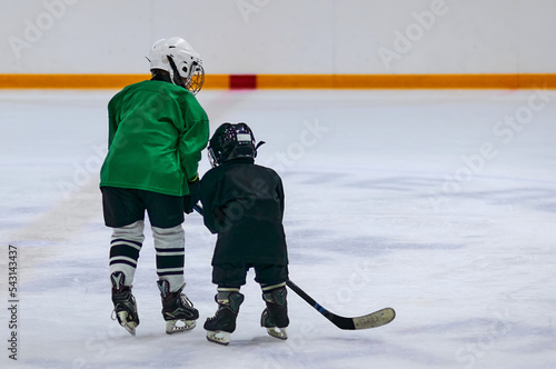 Two boys in hockey uniforms and protective helmets with hockey skates and a hockey stick standing on the ice of a large ice arena. Children in sports, young hockey players, champions concept.
