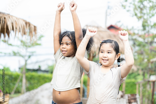 Happy African American child girl and Asian child girl playing wet mud and dirt on summer day. Children girl wet body and having fun with mud