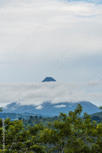 Paisaje de un día nublado donde se nota el Volcán arenal mostrando su cono en medio de un cúmulo de nubes