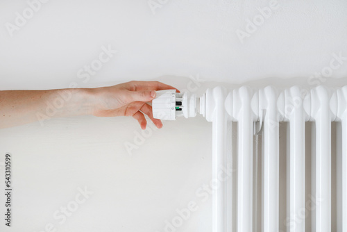Woman hand turning regulator knob on heating radiator in room
