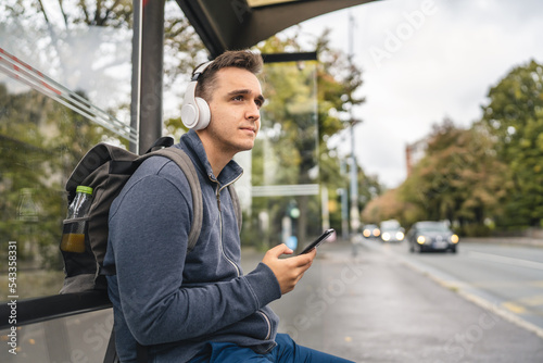 One man young adult male sit at public transport bus station waiting