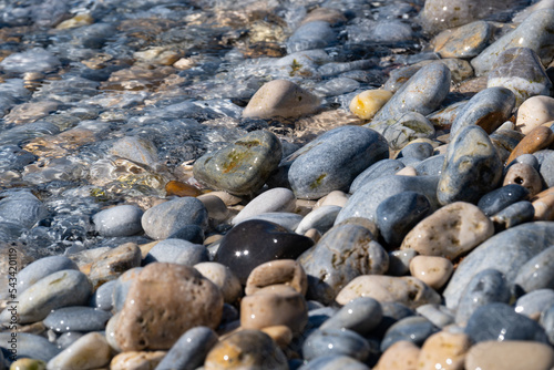 Clear transparent water of the Mediterranean shore flowing over colorful little stones on a beach in Samos