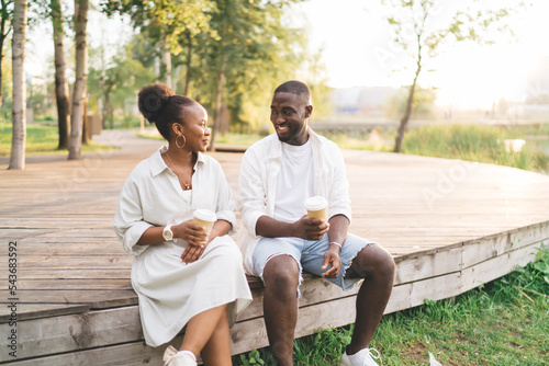 Cheerful black couple having conversation while sitting on wooden walkway