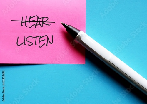 Pen and pink note on blue background with handwritten text HEAR changed to LISTEN, concept of practice active listening , focus and try to understand what speaker really want to communicate