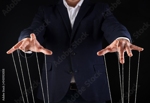 Man in suit pulling strings of puppet on black background, closeup