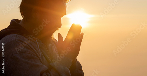 Close up portrait of young adult male with beard with praying hands praying for thank god golden sunset background. Concept of religion faith