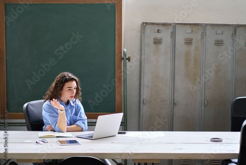 Young business woman, female online teacher looking at laptop talking leading hybrid conference online remote video call, virtual distance class in classroom or webinar web training working in office.