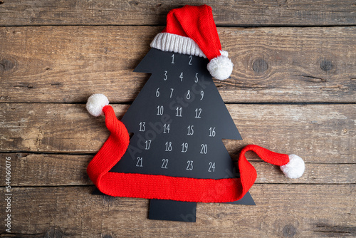 Christmas background. Advent calendar Christmas tree with Santa's hat on wooden table. Flat lay composition with advent calendar and Christmas decor