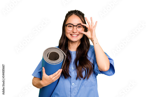 Young caucasian physiotherapist woman holding a mat isolated isolated on green chroma background excited keeping ok gesture on eye.