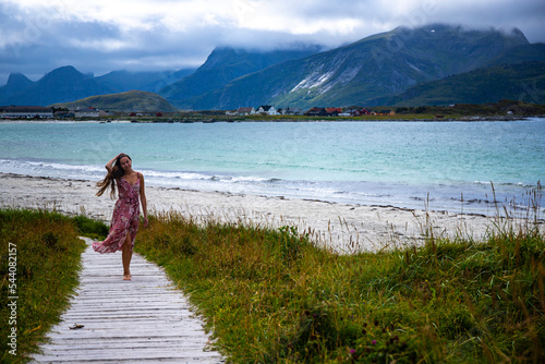 beautiful long-haired girl in a dress walks along the famous ramberg beach (rambergstranda) on the lofoten islands in northern norway; a beach holiday in the norwegian fjords