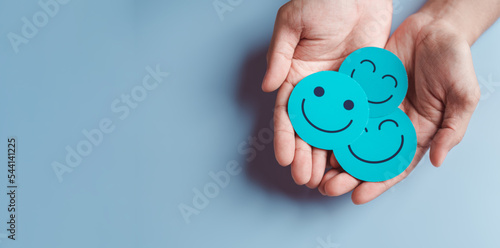 Hands holding blue happy smile face, good feedback rating, positive customer review, experience, satisfaction survey, smiley mental health, child wellness, world mental health day on blue background