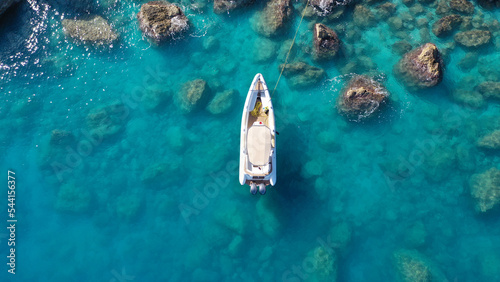 Aerial drone top down photo of white inflatable rib speed boat anchored in tropical exotic rocky bay with emerald sea