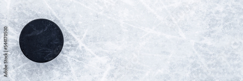Black old rubber puck on ice background. Closeup. Wide banner. Top down view. Empty place for text.