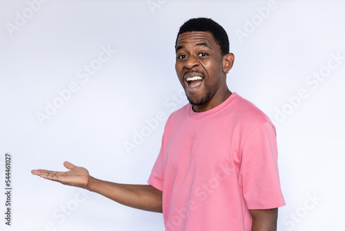 Portrait of excited African American man pointing at ads. Happy young male model with short dark hair in pink T-shirt looking at camera with open mouth, showing ad with palm. Advertisement concept