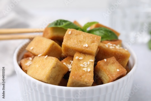 Bowl with delicious fried tofu, basil and sesame seeds on table, closeup