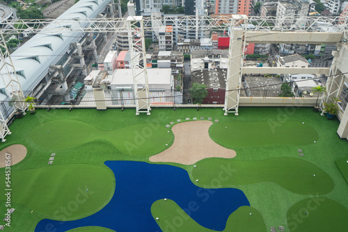 Small golf course of golf driving range on top of the roof with building backgound, architecture design of artificial green grass field , fake grass that separate zone color such as pond and sand.
