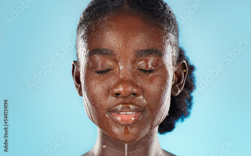 Water, skincare and face of a black woman in studio for health, wellness and self care with dermatology cosmetic care. African model on blue background cleaning or detox skin for beauty facial