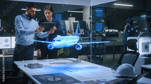 Aeronautics Factory Office Meeting Room: Engineer Holds Tablet Computer, Showing Augmented Reality Airplane Jet Engine to a Female Manager. Modern Industry 4.0 Research and Development Test.