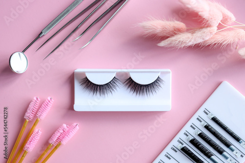 Tools for eyelash extension on trendy pastel pink background. False eyelashes, tweezers and brushes. Beauty shop. Makeup cosmetics. Top view, flat lay