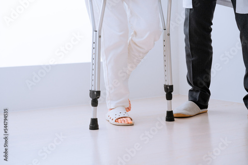 医者に介助されながら松葉杖をついて歩くミドル女性 リハビリイメージ