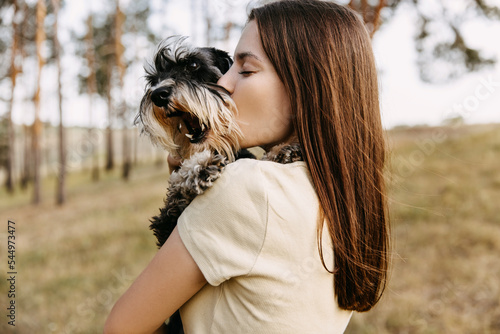 Young brunette woman hugging a miniature schnauzer breed dog, kissing it.