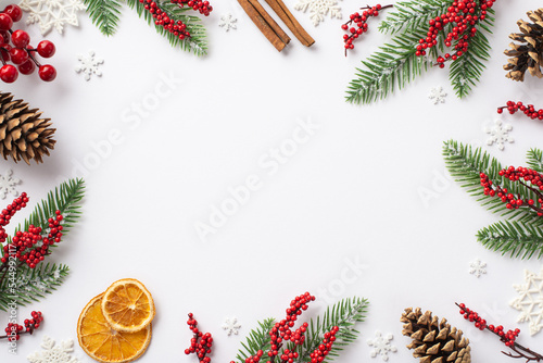 Christmas Eve concept. Top view photo of fir branches in frost mistletoe berries pine cones cinnamon sticks dried orange slices snowflakes on isolated white background with blank space in the middle