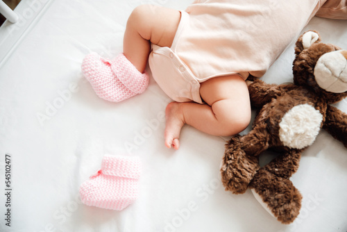 Newborn baby girl in knitted shoes with a bow in a сot on a white blanket. Baby lost shoes. Childhood concept.