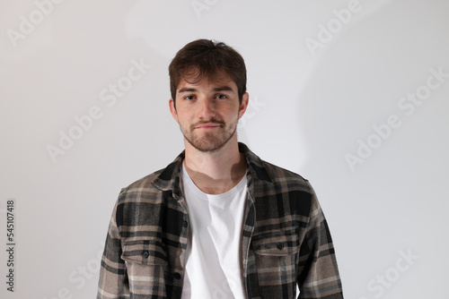 portrait d'un beau jeune homme de 25 ans debout, les mains dans les poches, portant une chemise. Sur fond gris