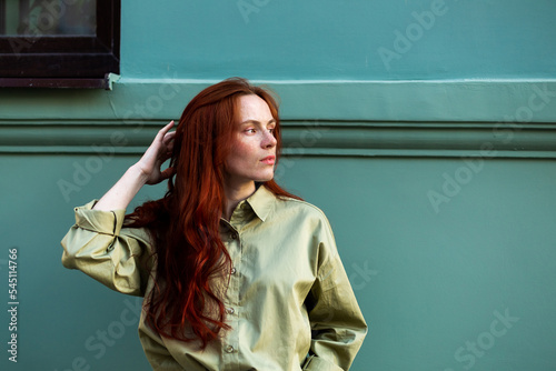 Young woman with long ginger hair outdoors in city. Young woman face with freckles