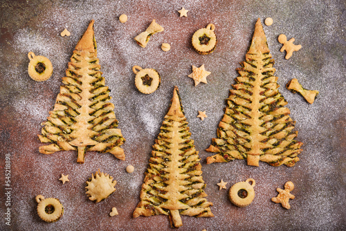 Christmas tree shape puff pastry pies with spinach, garlic and cheese, and puff pastry Linzer Christmas tree toys. Delicious homemade New Year savory baking. 