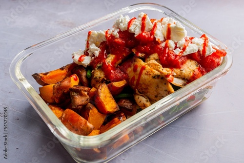 Fine shot of dish with chicken and squash pieces served with tomato sauce in pyrex on light surface