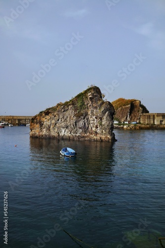 Vertical shot of a huge rock and a fishing boat in the Cantabrian sea in Cudillero in Asturia Spain