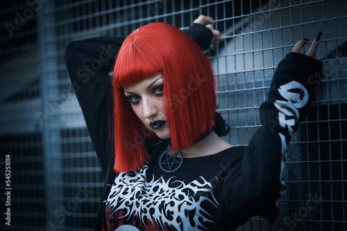 Young urban goth girl with a red hair wig posing outdoors, representing alternative subculture