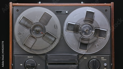 Vintage reel to reel tape recorder on black studio background. Retro music player with old plastic bobbins. Analog antique record player with magnetic tape reel for playing music. Front view close up.